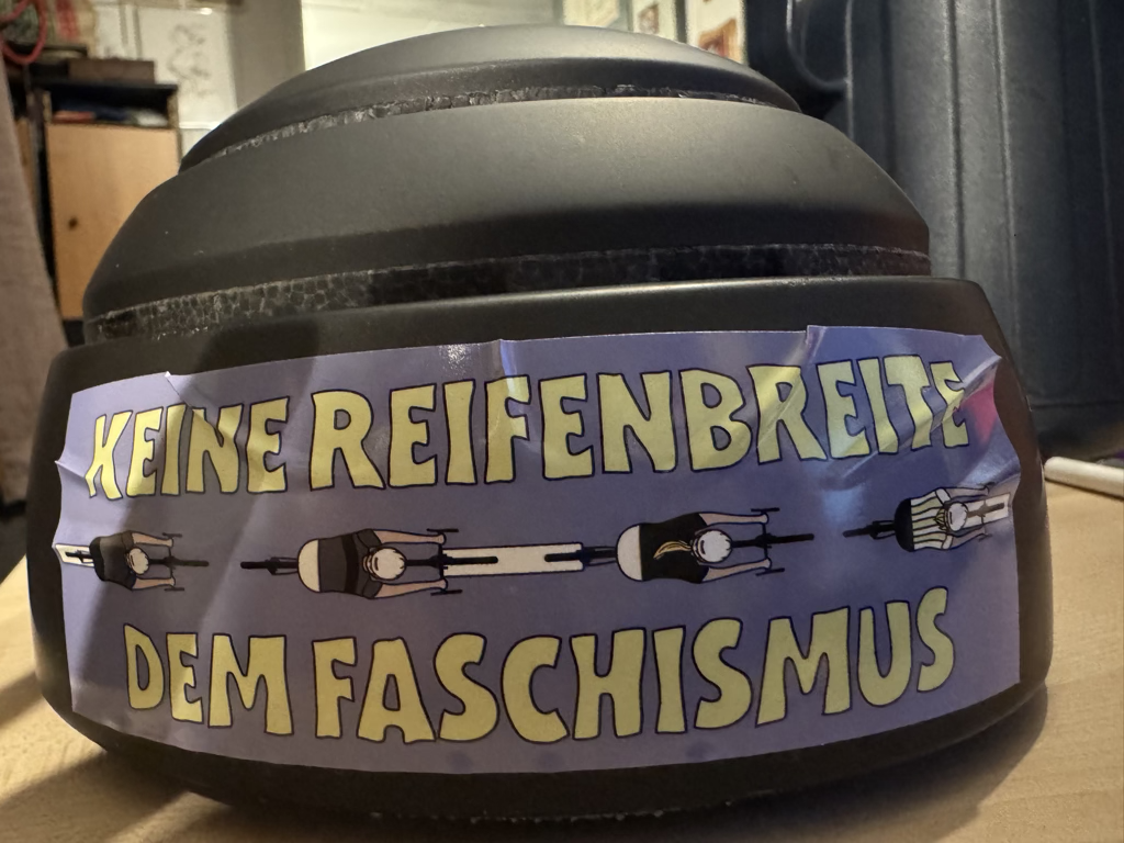 Schwarzer Closca-Fahrradhelm mit einem Aufkleber und der Aufschrift „Keine Reifenbreite dem Faschismus“.