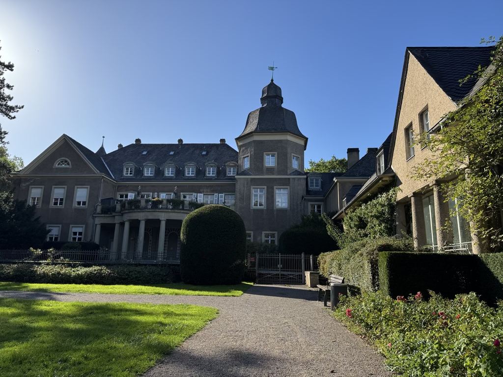 Herrenhaus von Schloss Garath mit neobarockem Turm, Vorplatz und gepflegtem Schlosspark bei Sonnenschein.